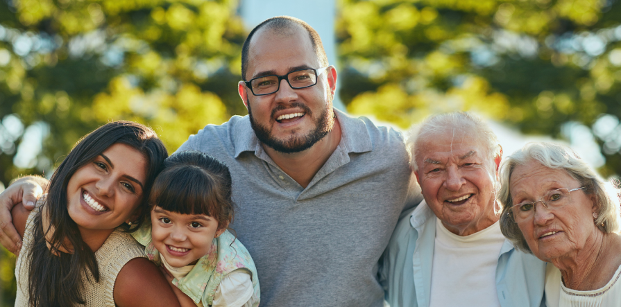 A smiling intergenerational family pose for the camera with arms around each other